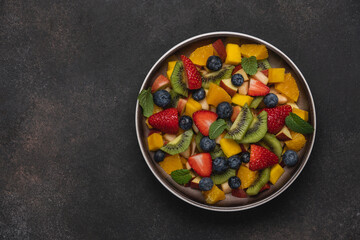 Fruit salad in bowl on brown background. Mango, kiwi, orange, apple, strawberry and blueberry berries