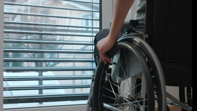 Man on wheelchair in living room looking through window. Handicapped invalid paralysed person, depressed alone at home.