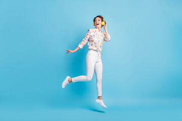 Fototapeta na wymiar Full size photo of young girl happy positive smile jump look empty space listen music earphones isolated over blue color background