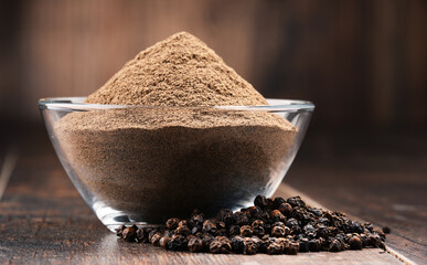 Composition with bowl of ground black pepper on wooden table