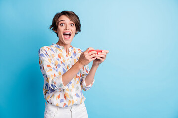 Photo of cheerful positive amazed young woman hold use phone gamer unbelievable win isolated on pastel blue color background