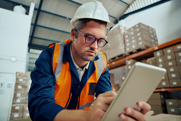 Portrait of a male warehouse worker looking at digital tablet screen in industrial warehouse