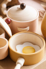 Children's tableware made of natural wood in pastel colors. Children's kitchen game, saucepan, cups, frying pan with scrambled eggs.