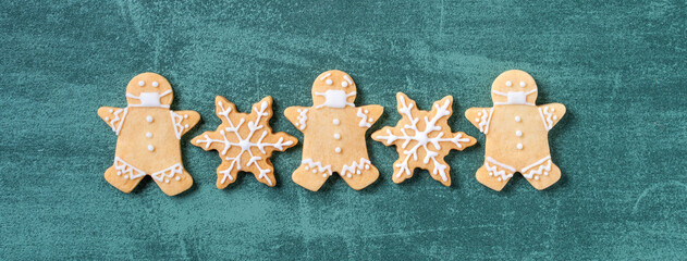 Top view of Christmas tree and snowflake cooikes with gingerbread man wearing mask.