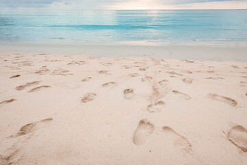 Fototapeta na wymiar Footprints on beautiful sandy beach and turquoise sea water at sunset time.