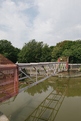 abandoned bridge without base bottom steel red over quay water river lake green with trees in the background