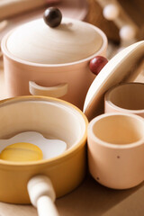 Children's tableware made of natural wood in pastel colors. Children's kitchen game, saucepan, cups, frying pan with scrambled eggs.