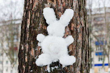 Handmade hare or rabbit made of white snow on the bark of a tree. Outdoor winter games, Christmas fun, Easter symbol