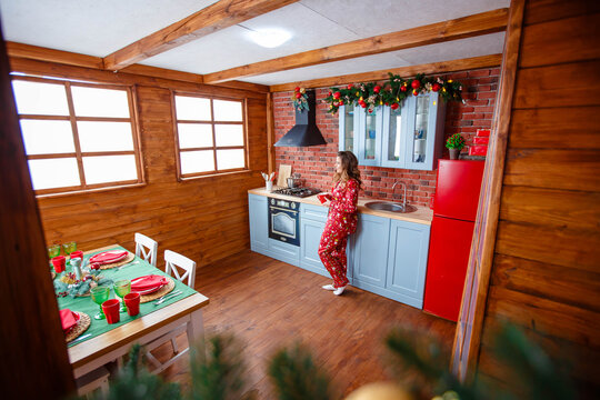 A beautiful girl in red New Year's pajamas holds a cup of tea in the kitchen. Christmas concept