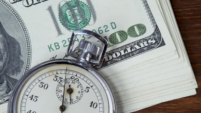 One hundred american dollars bills with analogue metal stopwatch. Counts time in business. Brown wooden background