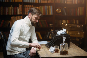 Thoughtful concerned male writer working on a novel on a typewriter, looking away, thinking about solving a problem in the home office, serious man looking for inspiration, feeling the lack of ideas