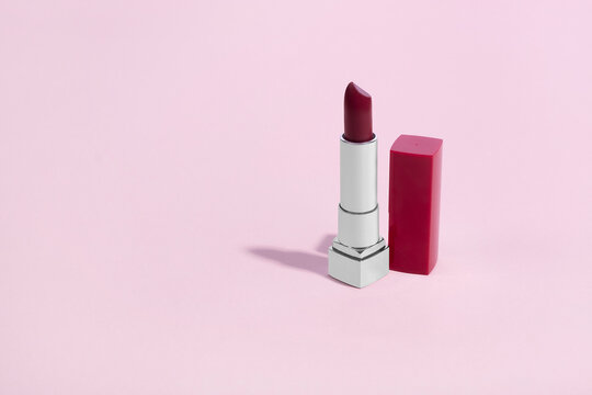 Red lipstick in a silver chrome tube next to matching red lid cap on a pink background with copy space and room for text with a right side composition