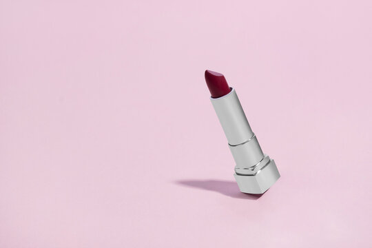 Red lipstick in a silver chrome tube tilted and falling on a pink background with copy space and room for text with a right side composition