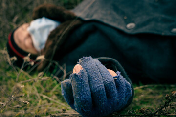 A homeless man in a medical mask lies unconscious on the wet ground. Poor dirty man lies dead on the ground