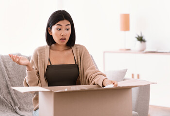 Frustrated asian woman unpacking wrong parcel, delivery mistake