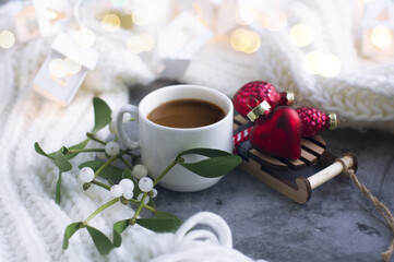 a cup of coffee, a toy wooden sled, a red heart, mistletoe sprigs, a knitted white scarf. Greeting card for new year, Christmas.
