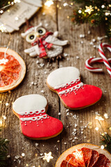 Christmas gingerbread cookies, fir branches, red decorations, lights garland, orange, candy on wooden background. Merry Christmas and New Year holiday. Xmas boots, close up, bokeh