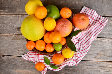 Different citrus fruits in a basket on a wooden background. decoration with red and white towel