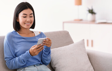 Smiling asian woman using smartphone at her home