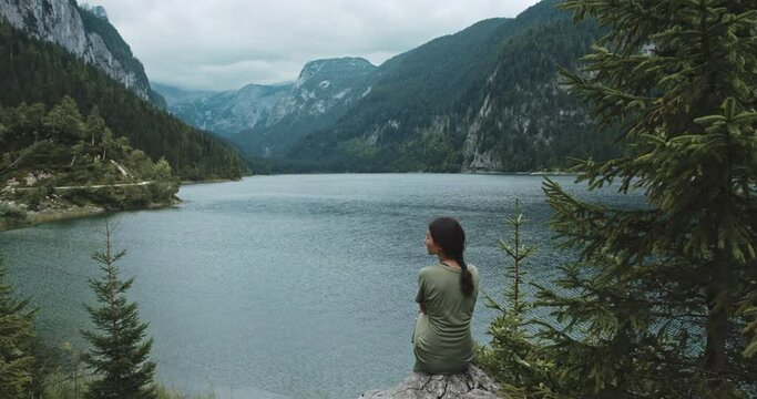 Young woman sitting on cliff in front of Breathtaking background. Girl enjoying moment, relaxing in magnifficent natural scene. Beautiful landscape of lake in mountains on sunny day. Concept of travel