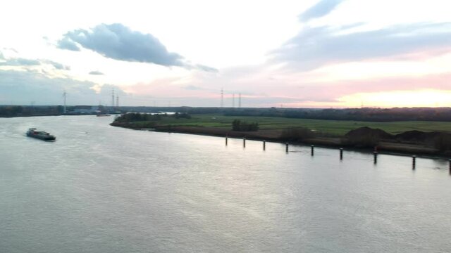 Drone lowering down over the river at sunset with a freight ship coming.