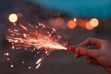 Young Man Lighting Up Firecracker in his Hand Outdoors in Evening. Guy Getting Ready for New Year Fun with Fireworks or Pyrotechnic Products - CloseUp Shot