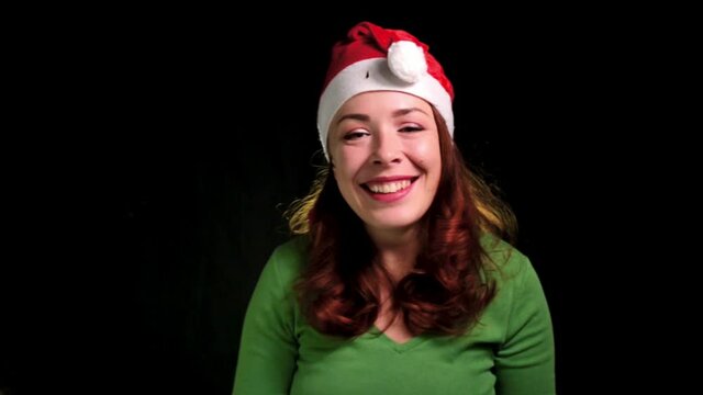 Woman in santa hat having fun, rejoices over colorful confetti on a dlack background