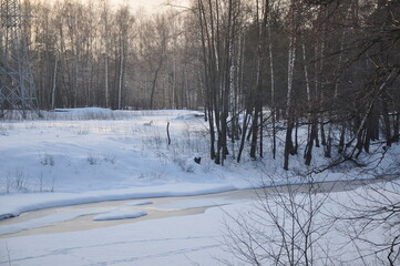 Snow-covered coast with trees and a river covered with ice in the setting sun