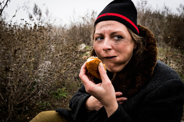 The poor dirty woman is eating a piece of bread.