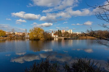 Prague, Czech Republic - November 30 2020: View of the Hamersky pond and church of Nativity of Mary and houses over the water with reflection of the blue sky and white clouds. Sunny autumn day.