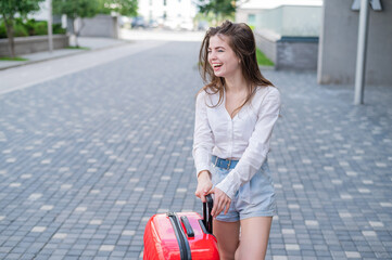 Beautiful caucasian woman goes on a trip with a red suitcase and waits for a taxi.