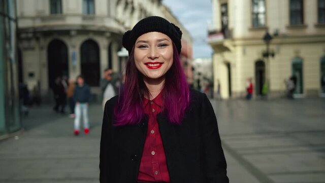 Attractive fashionable young woman walking in a beautiful street. Portrait of elegant asian girl wearing stylish black coat, red shirt, and attractive black cap. Concept of vogue and hipster lifestyle