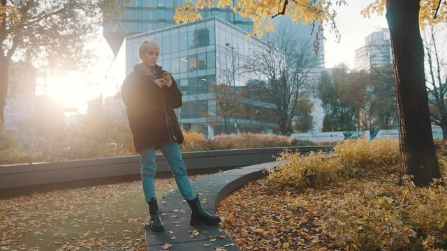 Young caucasian woman using phone in the city park in front of office building in autumn. High quality 4k footage