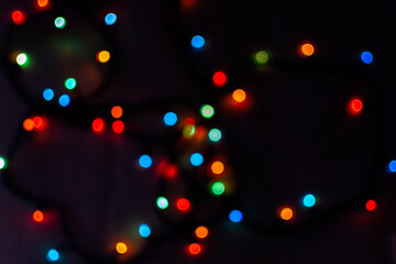 Multi-colored bokeh on a black background. Bright blurry textures of holiday lights. Colorful beautiful Christmas garlands on blurry background. Layout of a greeting card for the New year. Copy space