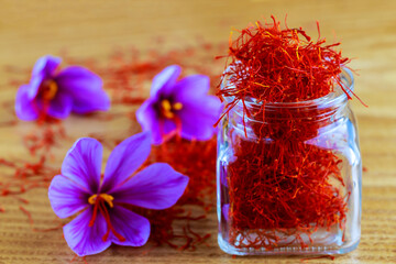 Stigmas of saffron are scattered on a wooden surface and in a glass bottle. Saffron crocus flowers....