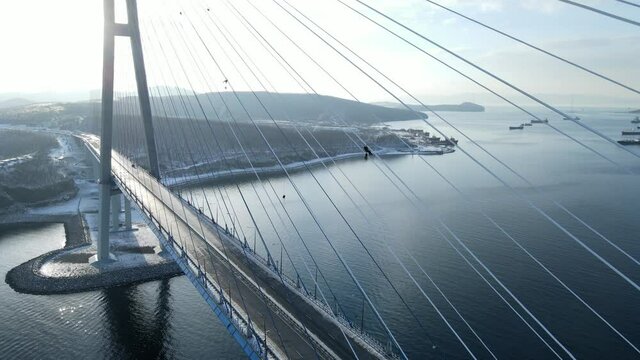 View from above. Closed Russian bridge due to icing of cables in Vladivostok. The camera flies off A group of climbers clear the ice from the shrouds against the background of the blue sea.