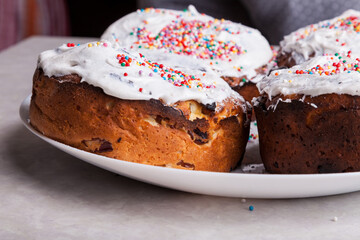 Close-up of freshly baked pastries on a plate in a home kitchen made of curd dough with raisins under a layer of white glaze - beaten egg whites with sugar, decorated with colorful confetti.
