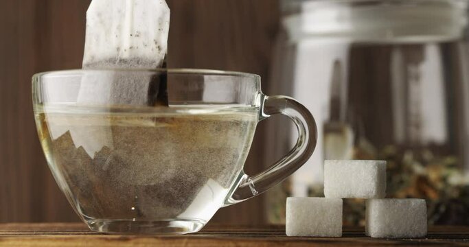The tea bag is brewed in a clear glass Cup with hot water closeup, slow motion. Next to it are pieces of refined sugar. A can of hand-picked herbal tea stands against a wooden background. Tea ceremony