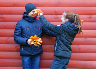 a happy girl and boy posing near red wooden wall and enjoys autumn