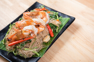 Shrimp, noodlesrice noodle and butter garlic fried shrimps sprinkled with pieces of chilli and chopped parsley on white dish on natural old wooden planks with spaghetti tongs, view from above, food
