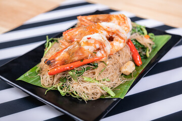 Shrimp, noodlesrice noodle and butter garlic fried shrimps sprinkled with pieces of chilli and chopped parsley on white dish on natural old wooden planks with spaghetti tongs, view from above, food
