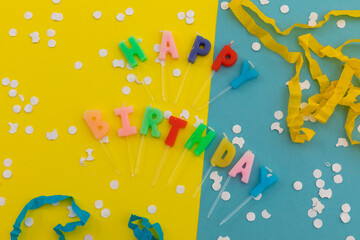 Happy birthday candles with confetti and party streamers on blue and yellow