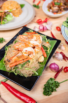 Shrimp, noodlesrice noodle and butter garlic fried shrimps sprinkled with pieces of chilli and chopped parsley on white dish on natural old wooden planks with spaghetti tongs, view from above, food