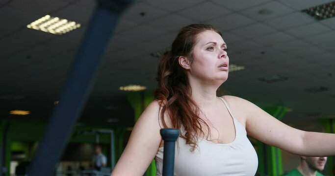 Portrait of the obese woman actively working out on the rowing machine in the green gym. Camera is moving left and right