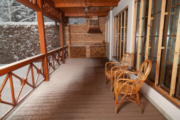 Two wicker chairs stand on veranda on winter day