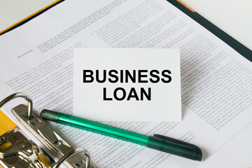 Text Business Loan on a white card that is in a folder with documents and a green pen