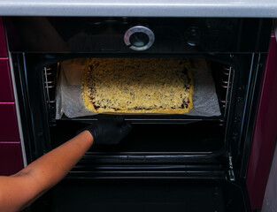 Obraz premium Women's hands in black gloves put a sweet cake in the oven for baking.