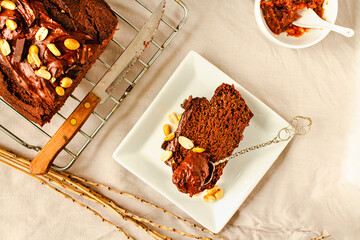 A piece of chocolate cake with nuts and milk chocolate cream frosting on white plate and light linen cloth. Top view