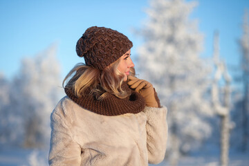 Young woman in a warm knitted hat and a snood in the winter forest