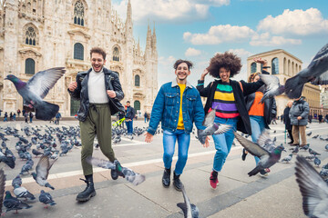 Group of four people friends running in Duomo Square in Milan, celebrating and laughing together having fun feeling free